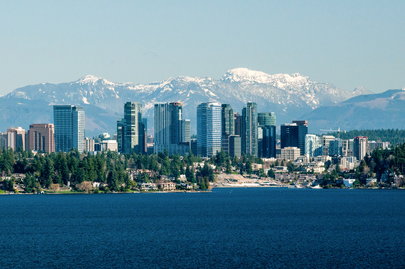 Skyline of Bellevue with the city buildings at the forefront and the mountains in the background.
